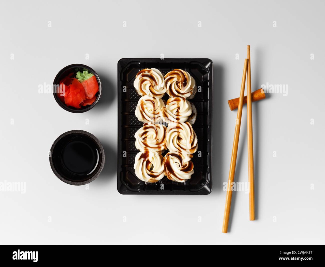 Sushi rolls with salmon, topped with cream cheese and sauce in a plastic package on a white background. Japanese, Asian cuisine, sushi delivery. Stock Photo