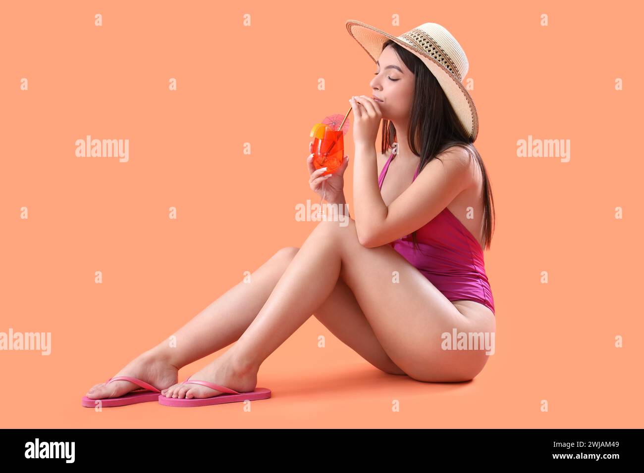 Beautiful young woman in swimsuit with glass of tasty aperol spritz sitting on orange background Stock Photo