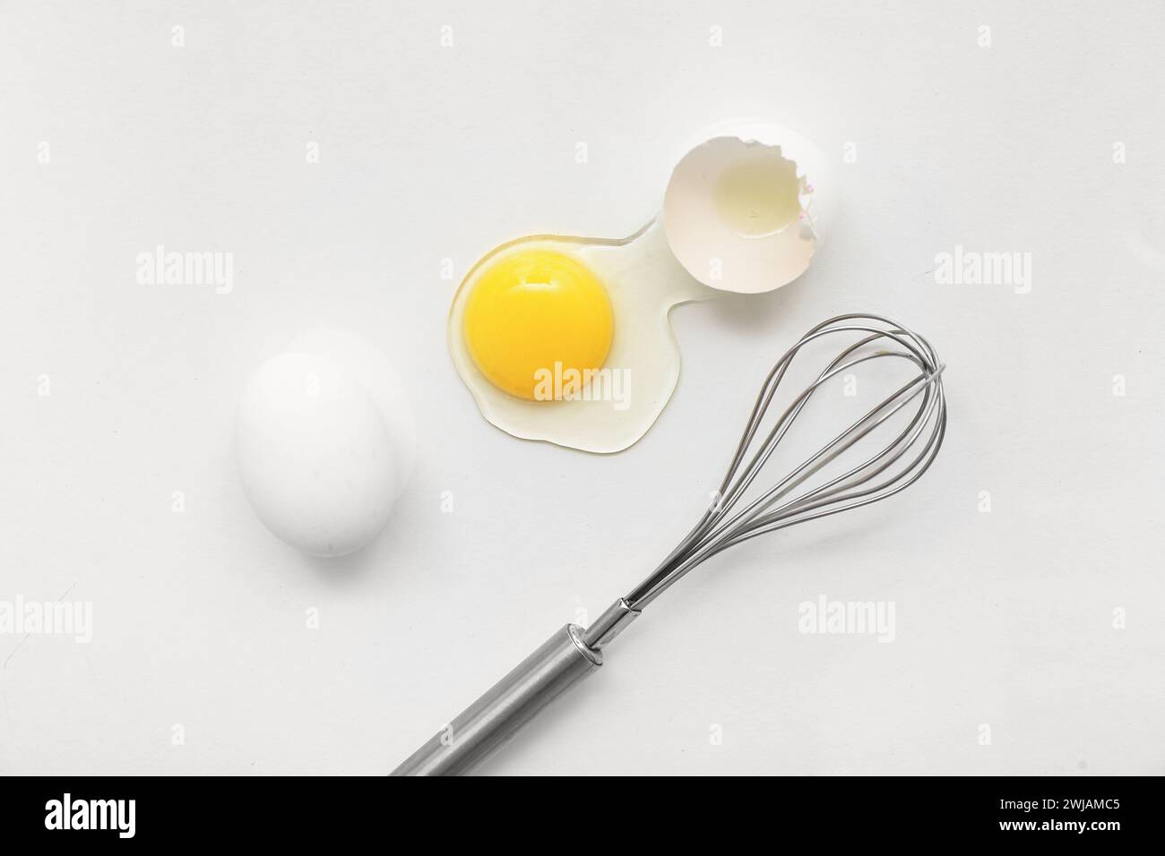 Cracked and whole chicken eggs with whisk on white background Stock ...