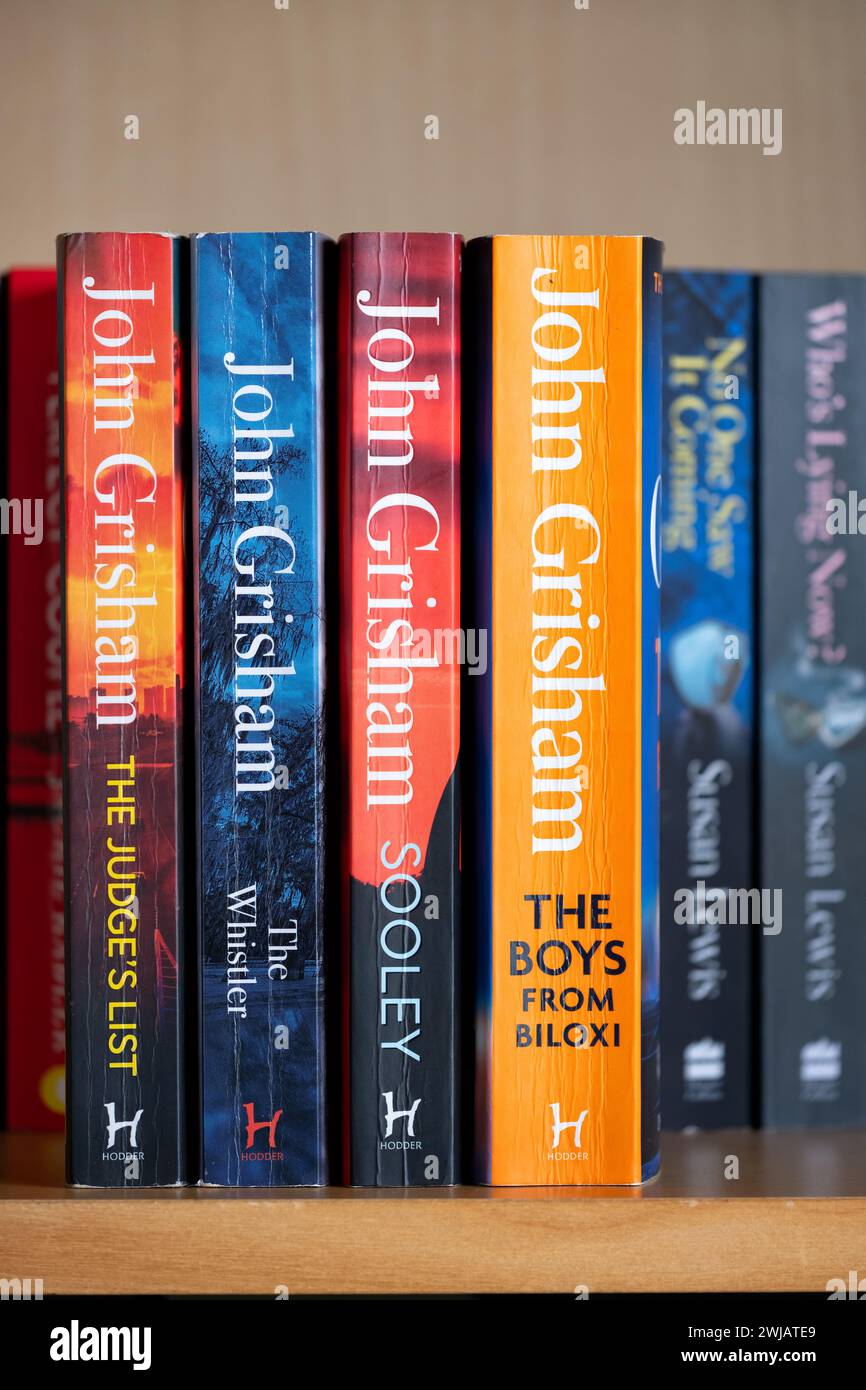 A domestic bookshelf with paperback books written by author John Grisham Titles including Sooley the Boys from Biloxi The whistler and the judges list Stock Photo