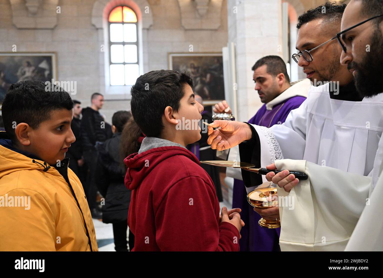 Bethlehem, West Bank. 14th Feb, 2024. A Palestinian Catholic boy receives holy communion during Ash Wednesday mass, the first day of Lent, in St. Catherine's Church in Bethlehem, West Bank, on Wednesday, February 14, 2024. Ash Wednesday marks the countdown to Easter with prayer, fasting and vowing devotion to God. Photo by Debbie Hill/ Credit: UPI/Alamy Live News Stock Photo