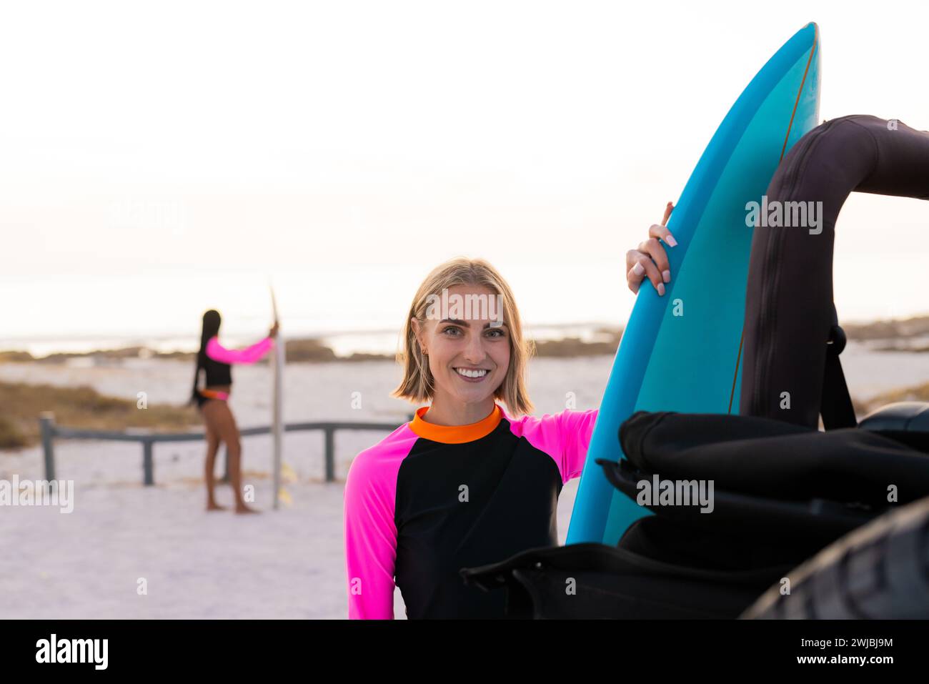 Young Caucasian woman smiles holding a surfboard Stock Photo