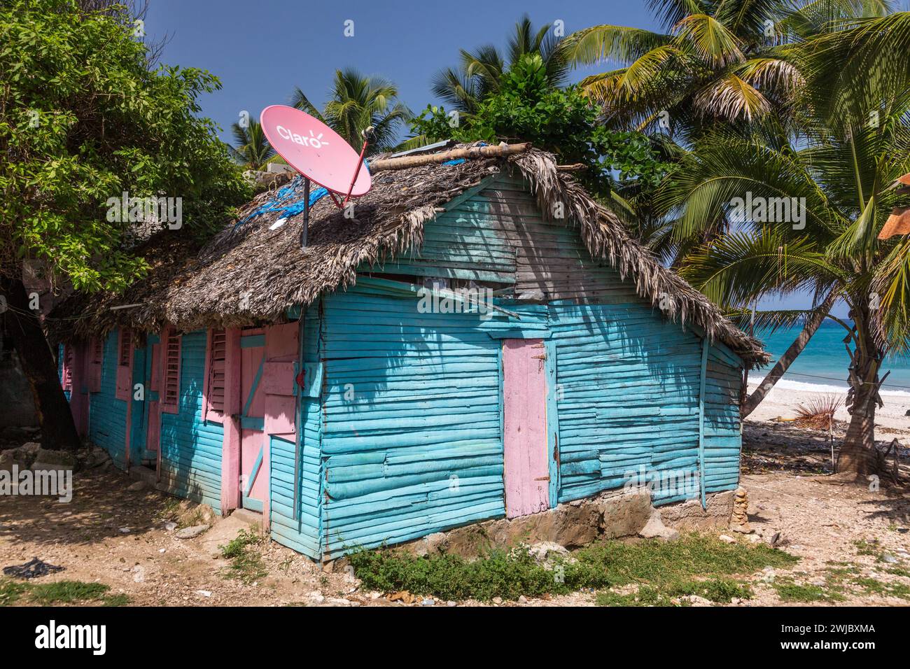 A small, traditional wooden slab house with a rpalm thatch roof  and satellite dish in the rural Dominican Republic. Stock Photo