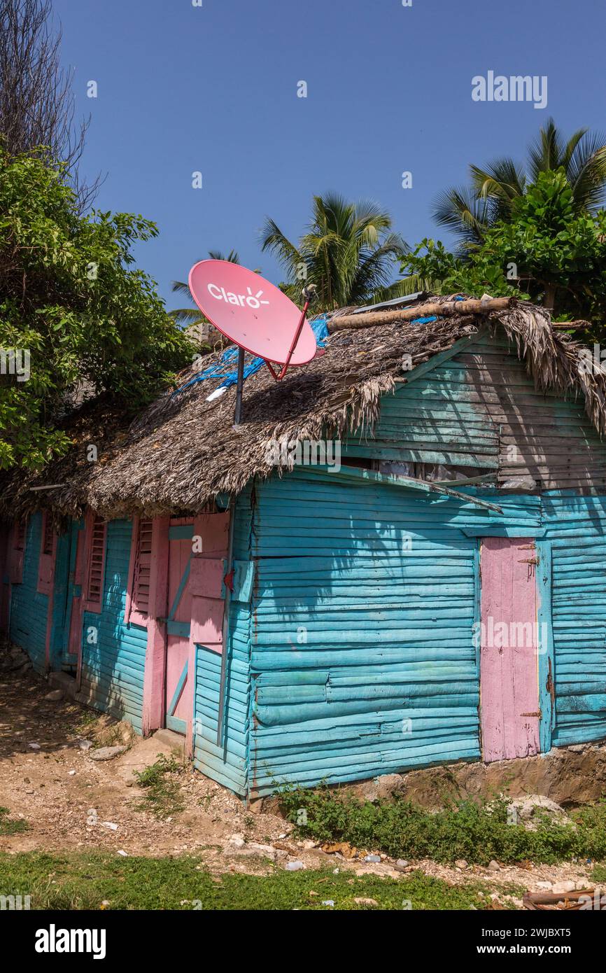 A small, traditional wooden slab house with a rpalm thatch roof  and satellite dish in the rural Dominican Republic. Stock Photo