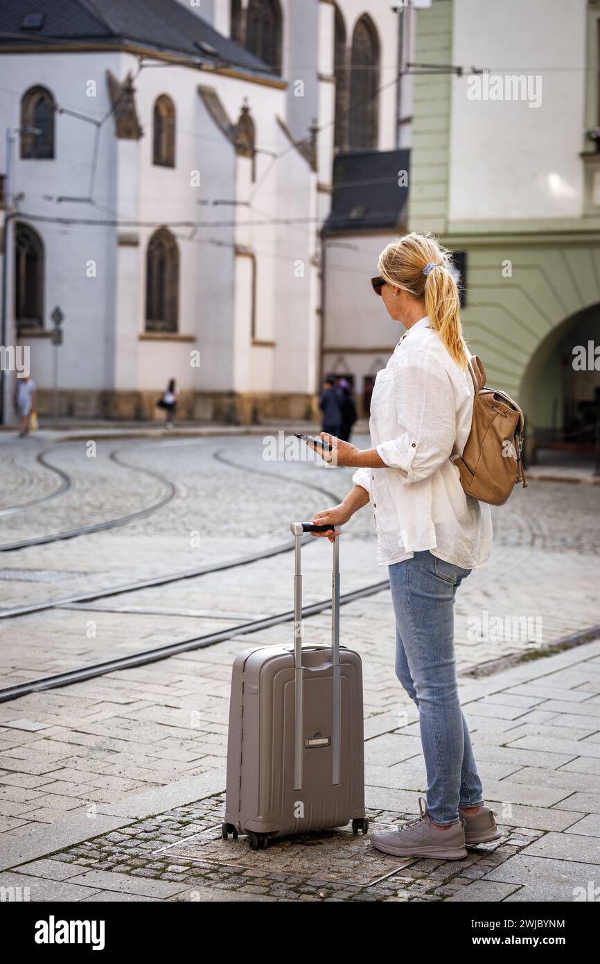 Woman tourist with suitcase waiting for tram on street. Travel and public transportation in European city Olomouc, Czech Republic Stock Photo