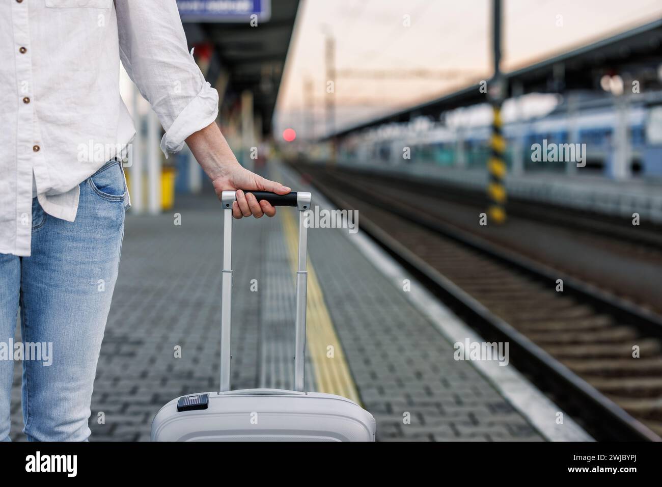 Woman tourist with suitcase is waiting for train at railway station. Solo travel concept Stock Photo