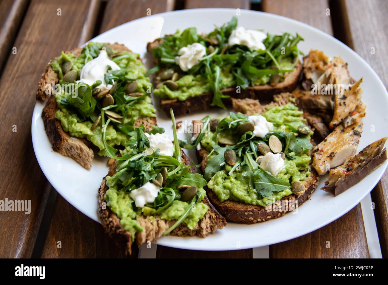 Smashed avocado on Toast with Labneh, Lemon, Parsley, Cheese, Edamame and different dried seeds, sunflower and pumpkin, very healthy and vegan snack Stock Photo