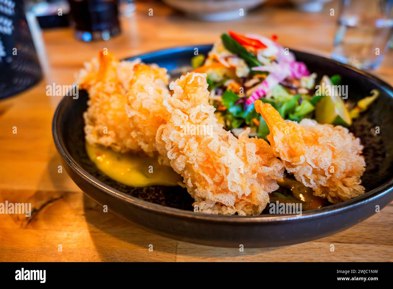 Fried tempura shrimp with mango sauce and salad in bowl on table with glass of water. Stock Photo