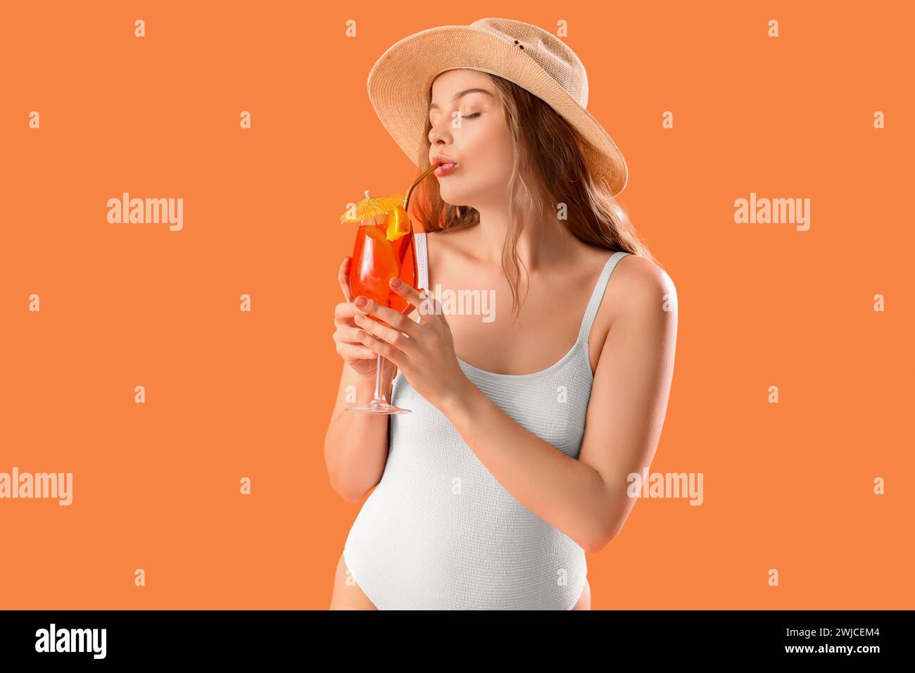Beautiful young woman in swimsuit drinking tasty aperol spritz on orange background Stock Photo
