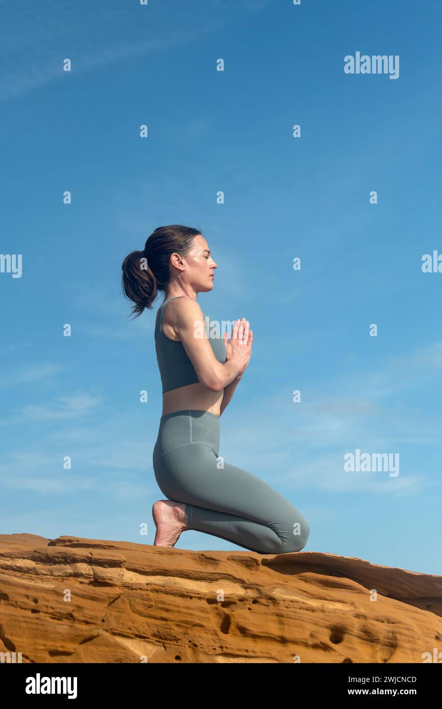 woman kneeling and meditating on rocks outside, blue sky background Stock Photo