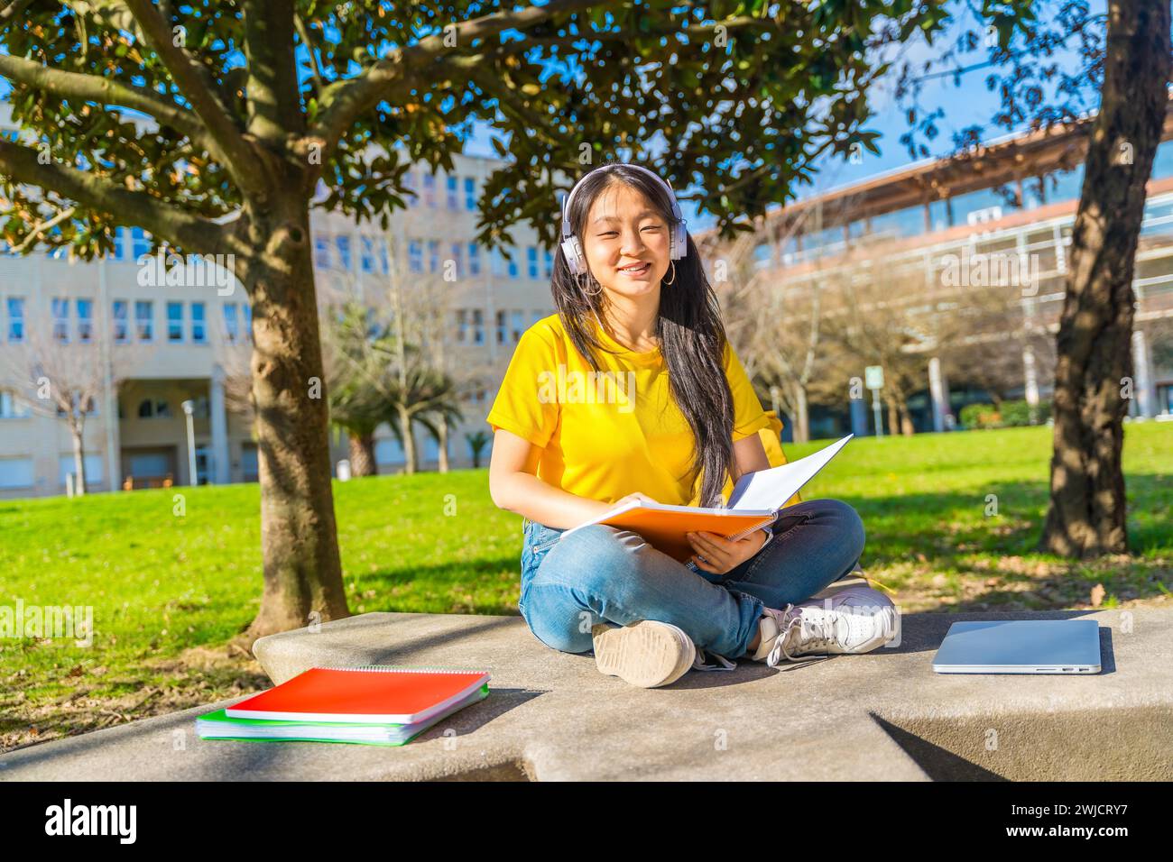 Portrait of a smiling chinese woman sitting on the campus reading notes and studying Stock Photo