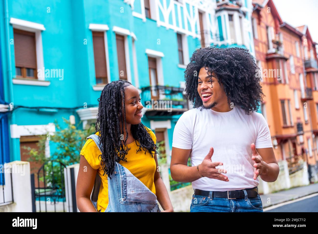 Two happy young african friends talking while visiting a city street with colorful houses Stock Photo