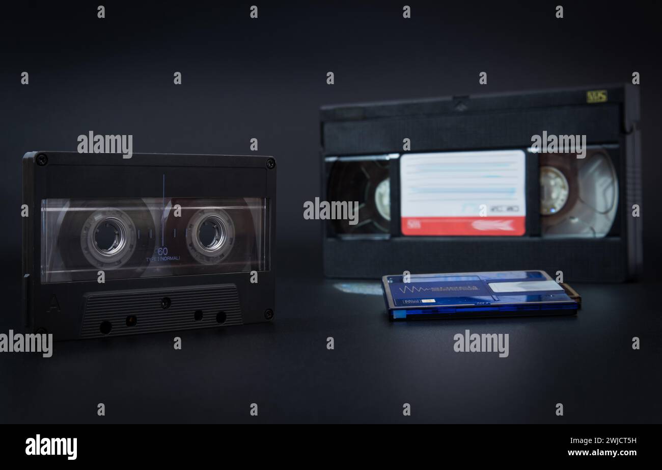 A vintage cassette tape and a VHS tape side by side on a grey background, audio cassette, video cassette, minidisc audio Stock Photo