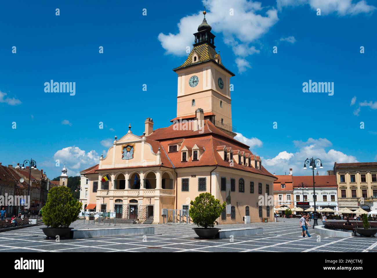 A busy town square with a town hall and a large clock on a clear day, Old Town Hall at Piata Sfatului Market Square, Old Town, Brasov, Brasov Stock Photo