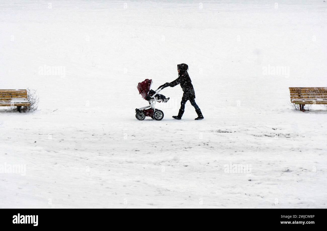 A woman pushes a pram through a snow-covered park in the freezing cold, Berlin, 09/02/2021 Stock Photo