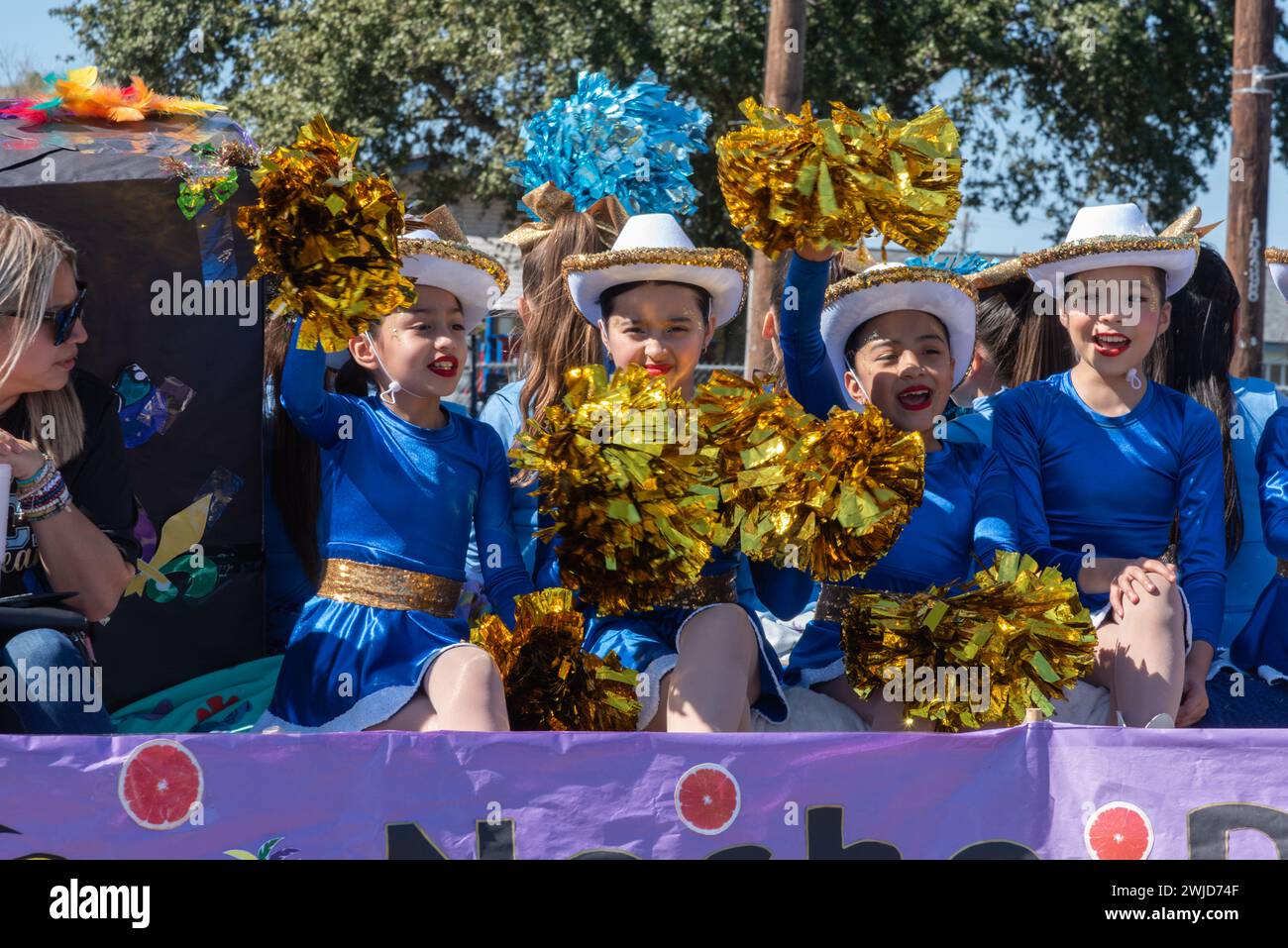 Young girls wearing cowboy hats, waving gold pom poms ride on a float in  2024 Parade of Oranges, part of 92nd Texas Citrus Fiesta, Mission, Texas USA. Stock Photo