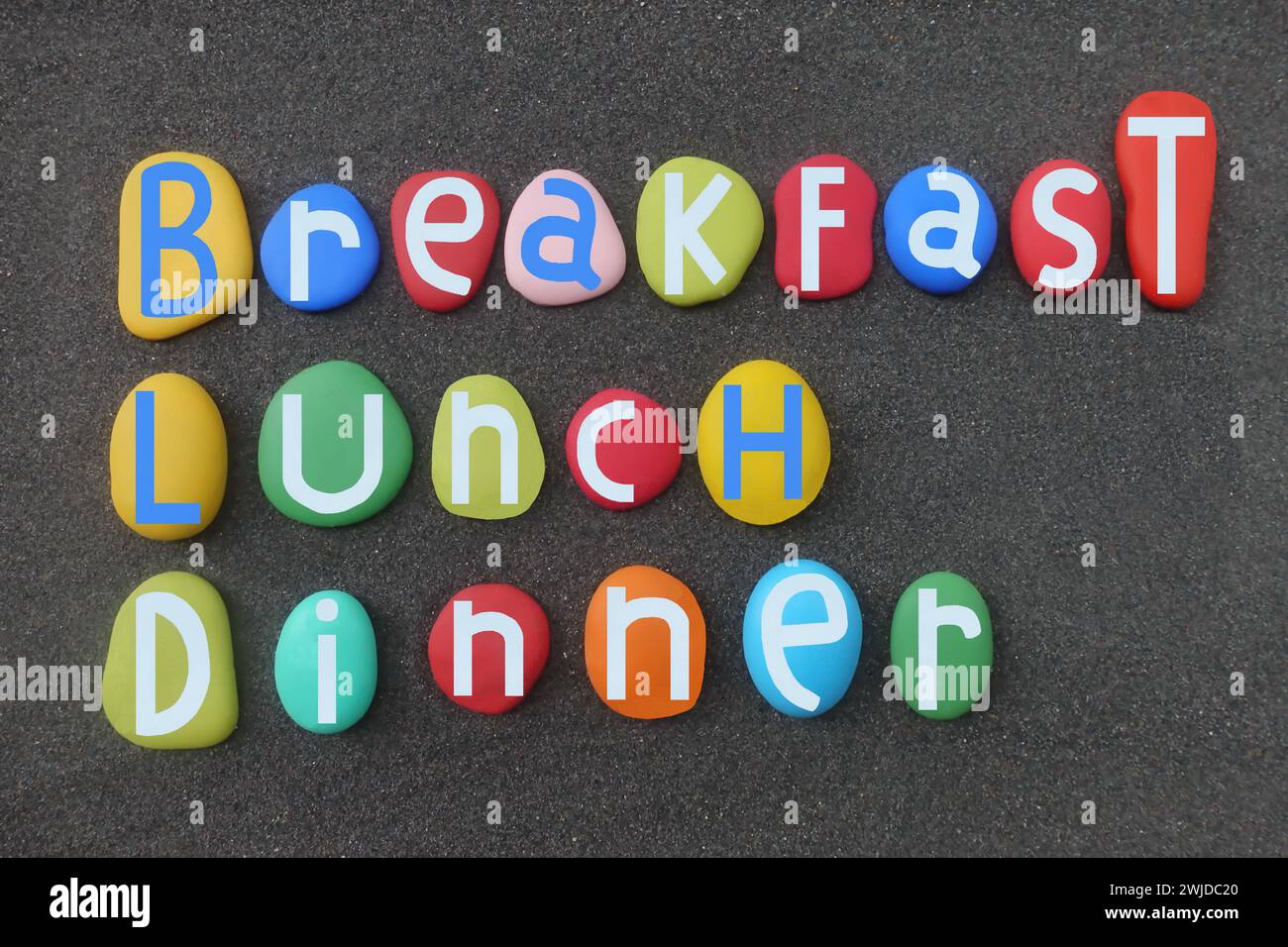 Breakfast, lunch, dinner, creative text art composed with hand painted multi colored stone letters over black volcanic sand Stock Photo