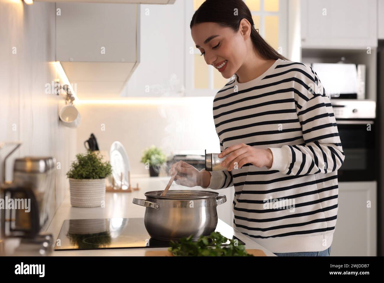 Smiling woman adding spices into pot with soup in kitchen Stock Photo