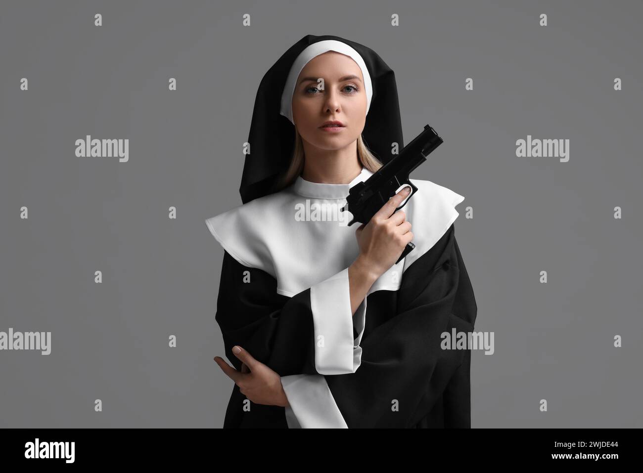 Woman in nun habit holding handgun on grey background Stock Photo