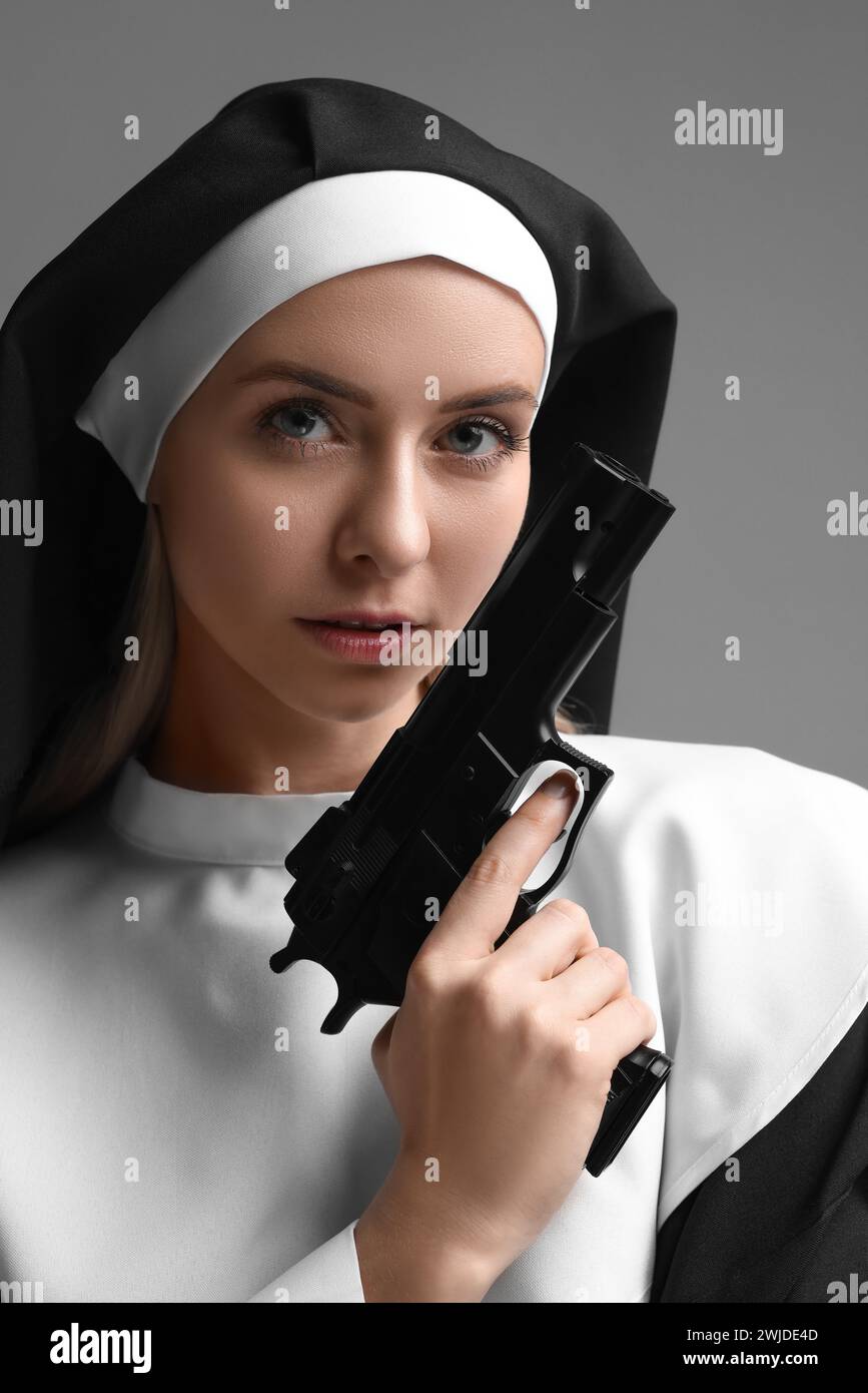 Woman in nun habit holding handgun on grey background, closeup Stock Photo