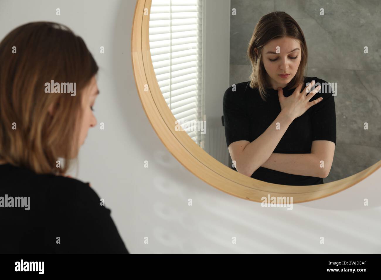 Sad young woman near mirror in room Stock Photo