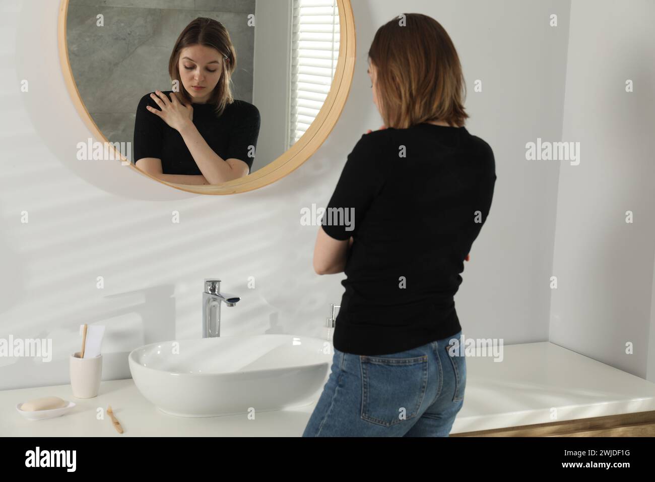 Sad young woman near mirror in bathroom Stock Photo