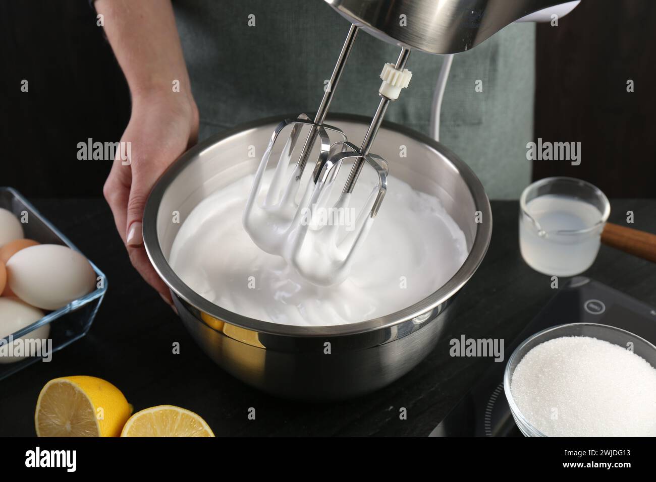 Woman making whipped cream with hand mixer at black table, closeup