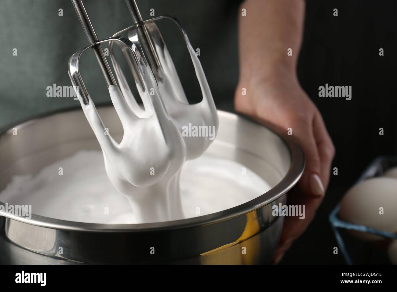 Woman making whipped cream with hand mixer on black background, closeup