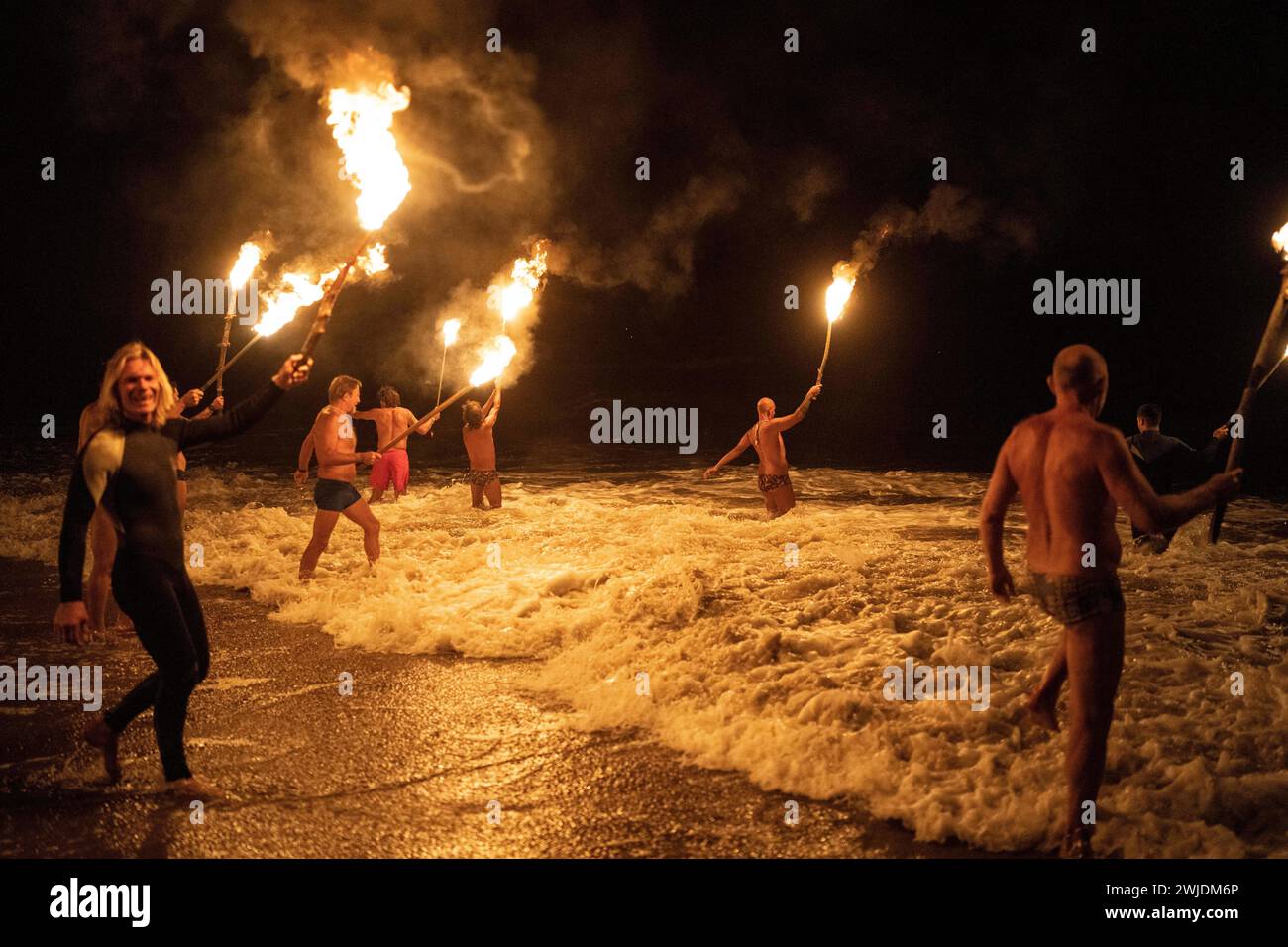 Lifeguards carry torches as they wade into the ocean in a ceremony to ...