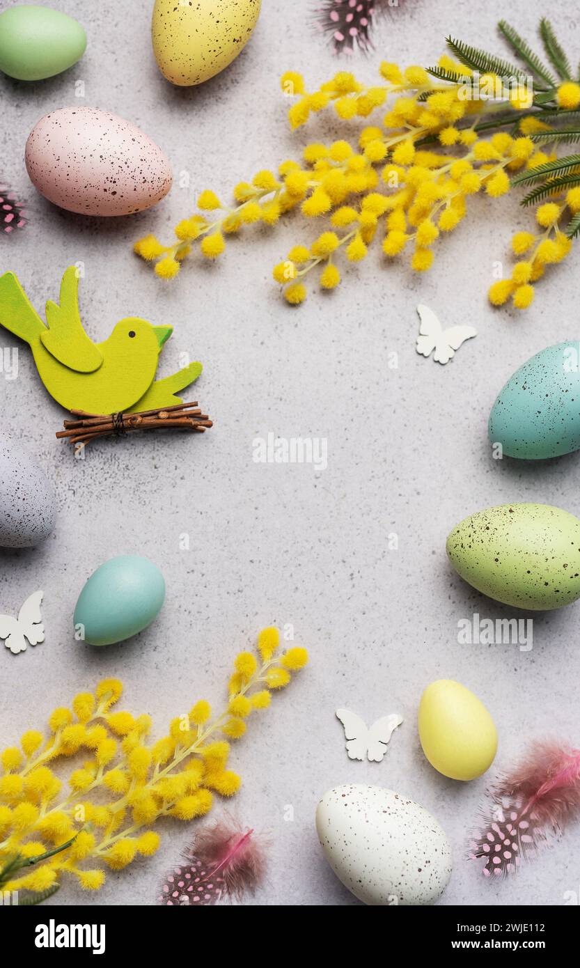 Decorative Easter composition featuring pastel-colored eggs, vibrant mimosa branches, and festive cutouts on a light, textured surface. Stock Photo