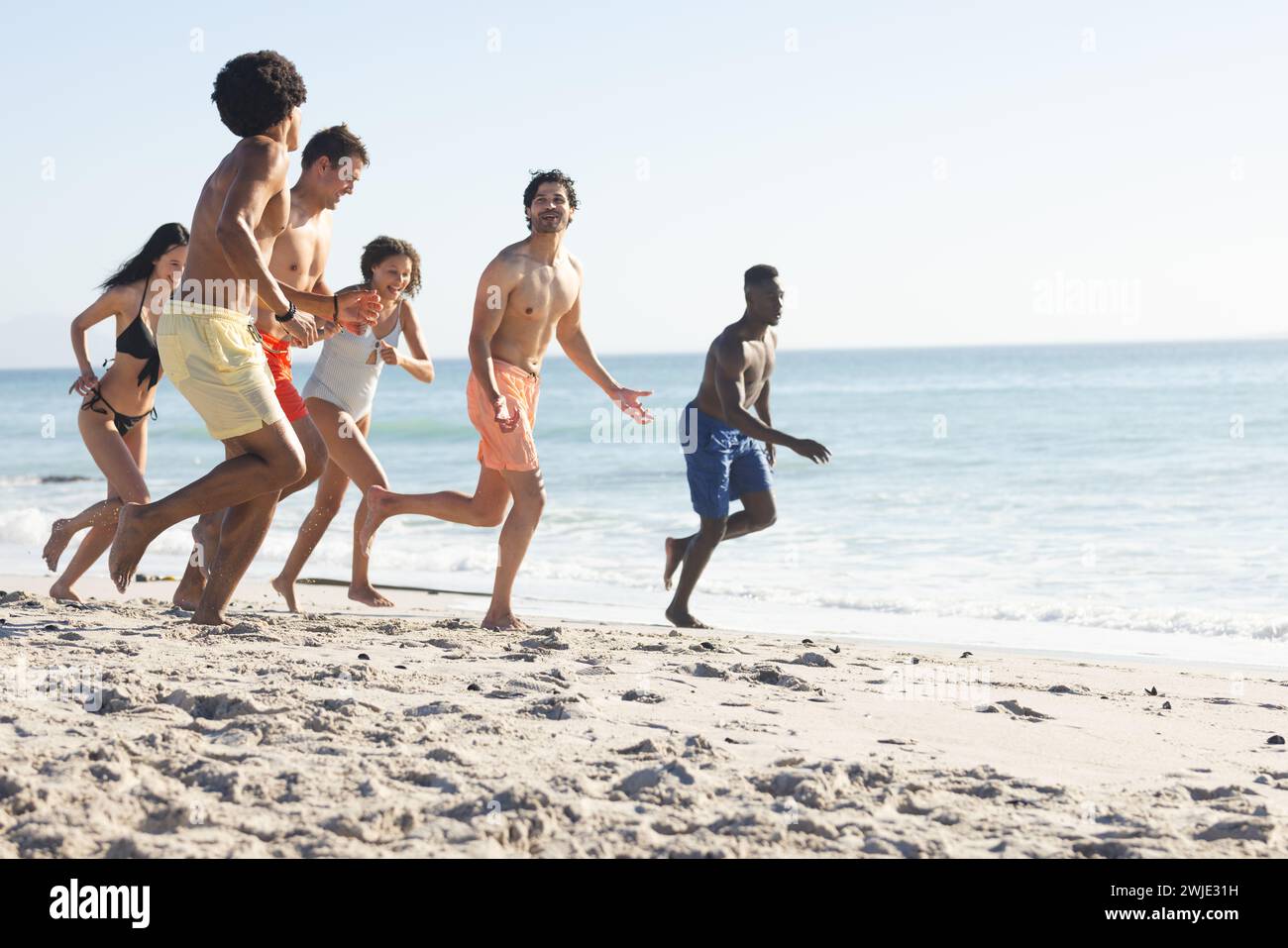 Diverse friends enjoy a lively race on a sunny beach, with copy space Stock Photo