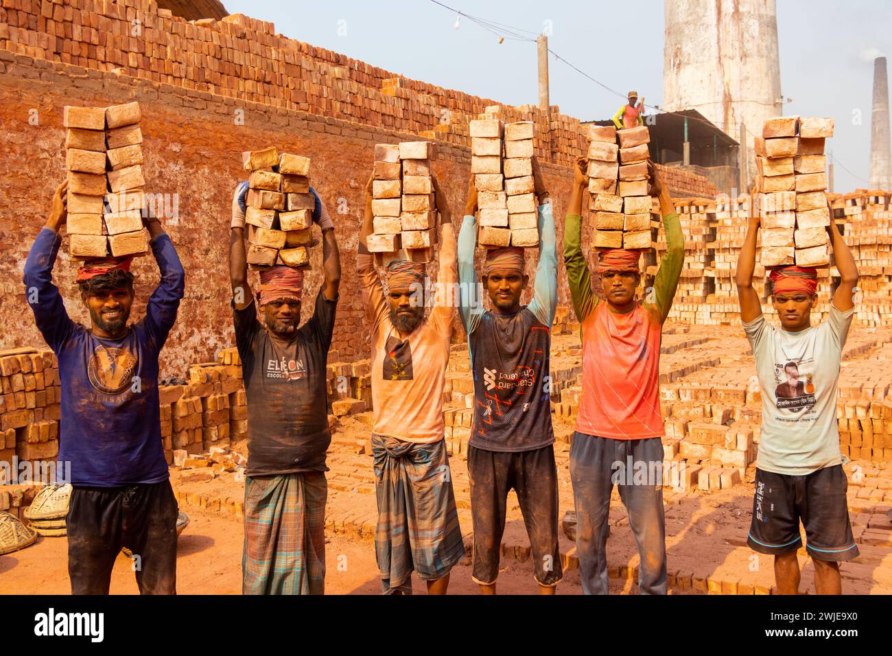 Dhaka, Dhaka, Bangladesh. 15th Feb, 2024. Workers carry piles of bricks weighing more than 20 kg on their heads in a kiln in Dhaka, Bangladesh. The labourers ''“ who are paid less than Â£1 a shift ''“ move up to 2,500 bricks a day in sweltering conditions. Around 4, 00,000 low-income migrants arrive in Dhaka from different parts of the country every year to work at brickfields. Long working hours under the scorching sun in the brick fields, massive accumulation of dust, the risk of falling from the trucks and piles of bricks, and carrying excessive loads pose serious health hazards for the w Stock Photo