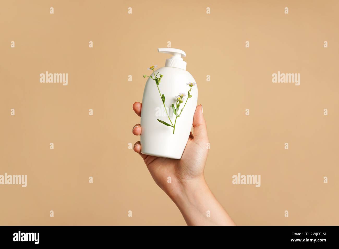 Female hand with white cosmetic bottle and flowers on beige background Stock Photo