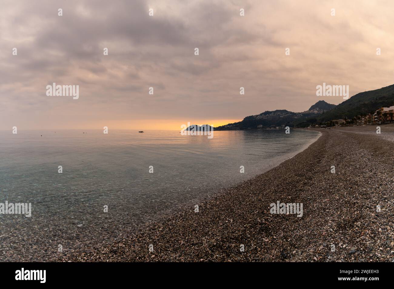 A view of the stone pebble beach and clear water at Letojanni on Sicily at sunsest Stock Photo