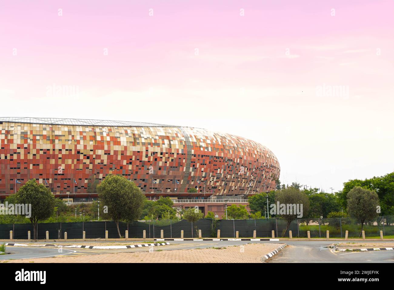 The iconic Soccer City Stadium in Johannesburg basks in the warm glow of a sunset, showcasing its distinctive mosaic facade against the evening sky. Stock Photo