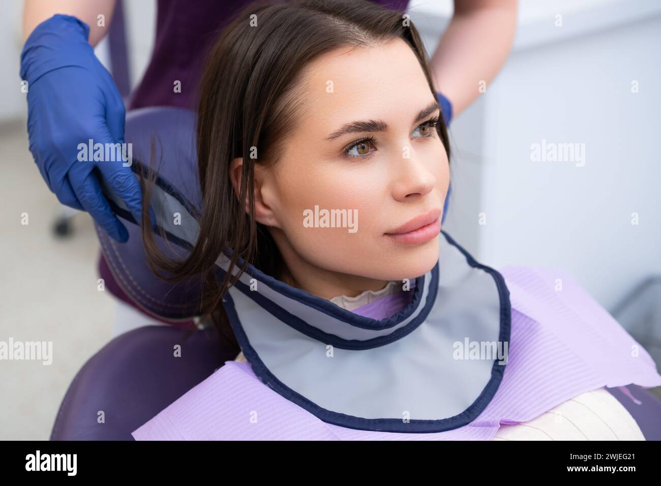 The dental assistant outfits the patient with a protective neck shield ...