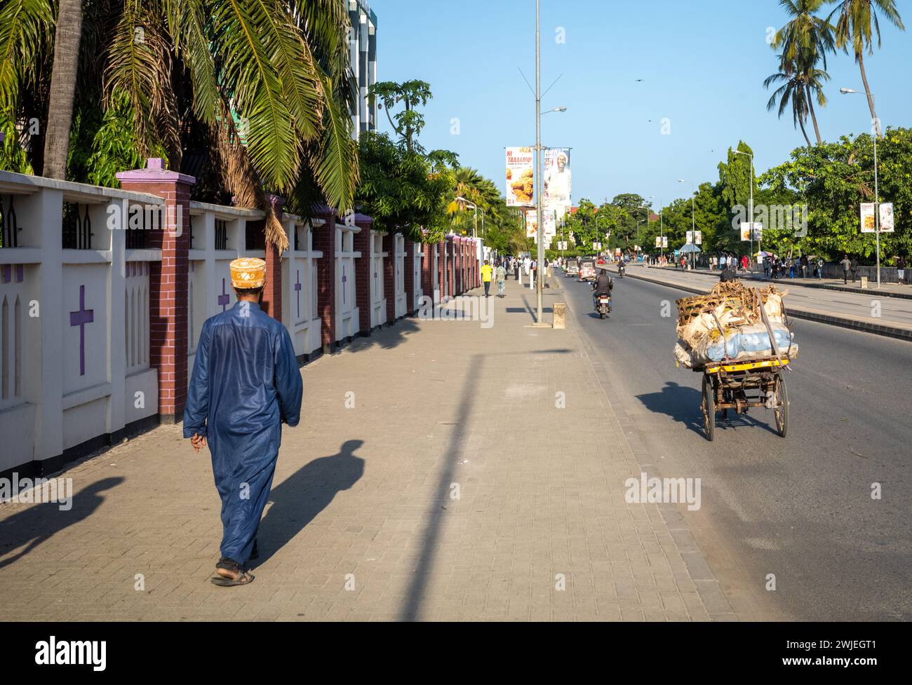 A muslim man wearing a traditional kanzu long tunic and kofia cap walks past the Azania Front Cathedral in Dar es Salaam, Tanzania. Stock Photo