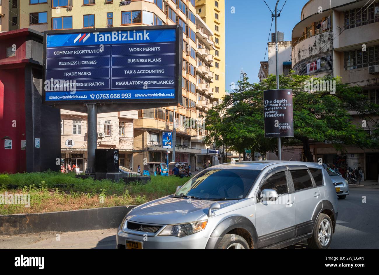 Cars on a roundabout go past a hoarding advertising business regiatration, planning and tax services in Dar es Salaam, Tanzania. Stock Photo