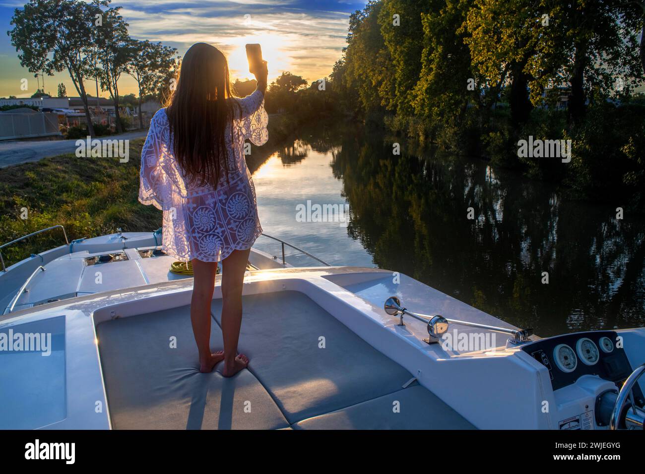 Girl in the sunset on the deck of a boat. Canal du Midi near Carcassonne Aude South of France southern waterway waterways holidaymakers queue for a bo Stock Photo