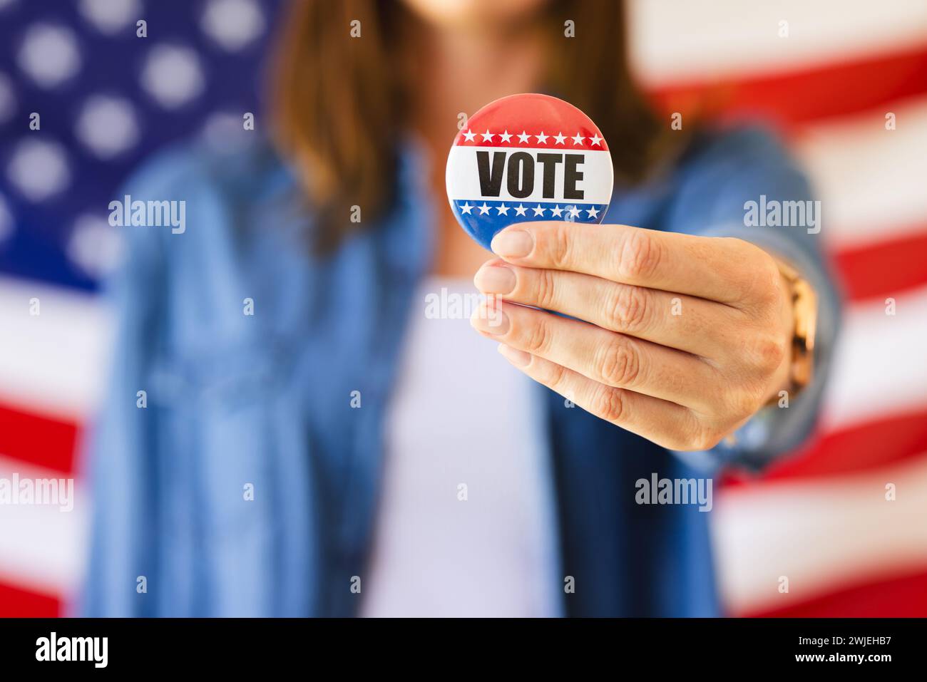 A caucasian woman is holding out a vote badge towards the camera, with copy space unaltered Stock Photo