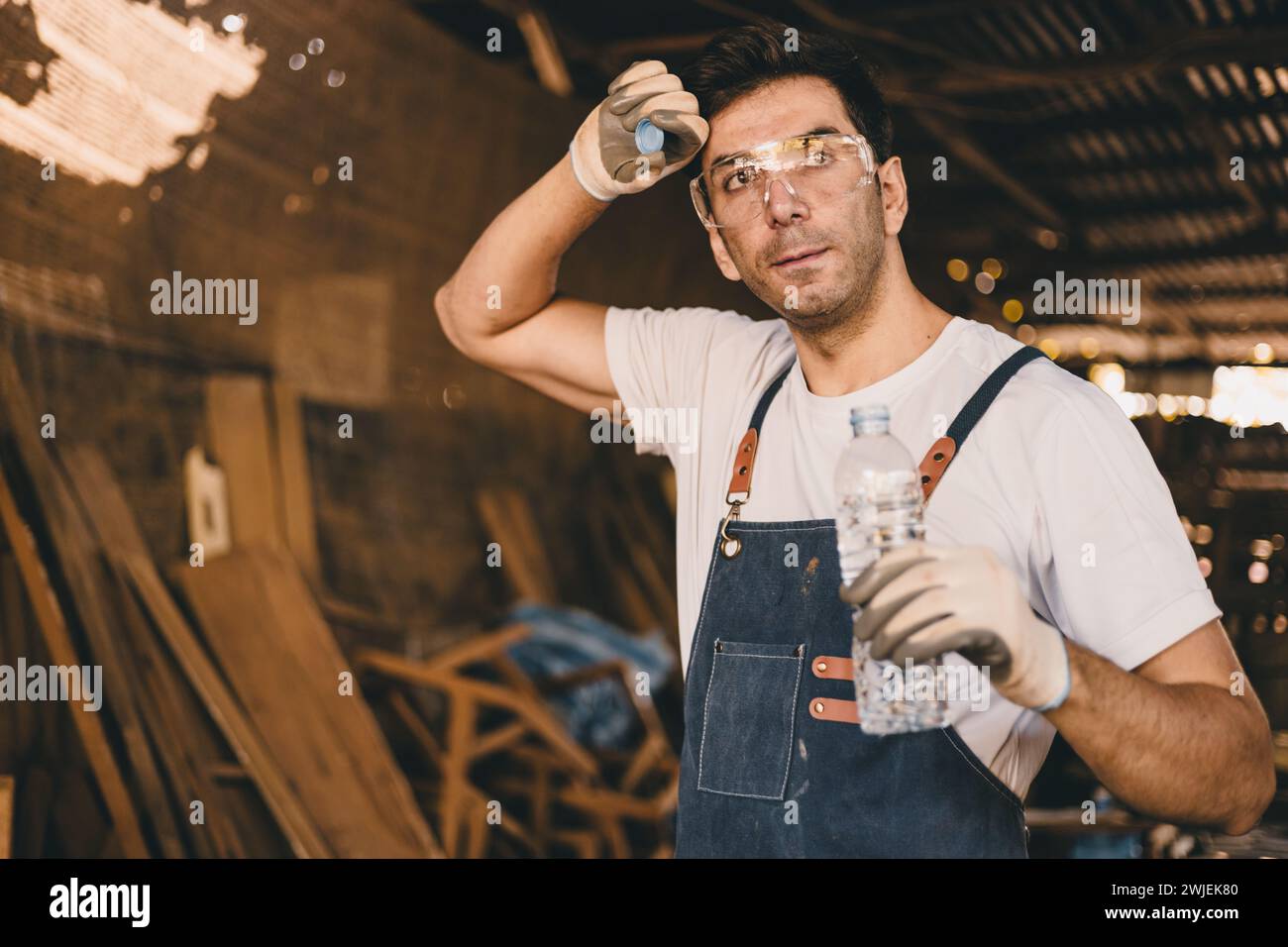 Tired stress carpenter man worker sweating hot workplace hardwork drinking water brake relax dehydrate in wood furniture workshop. Stock Photo