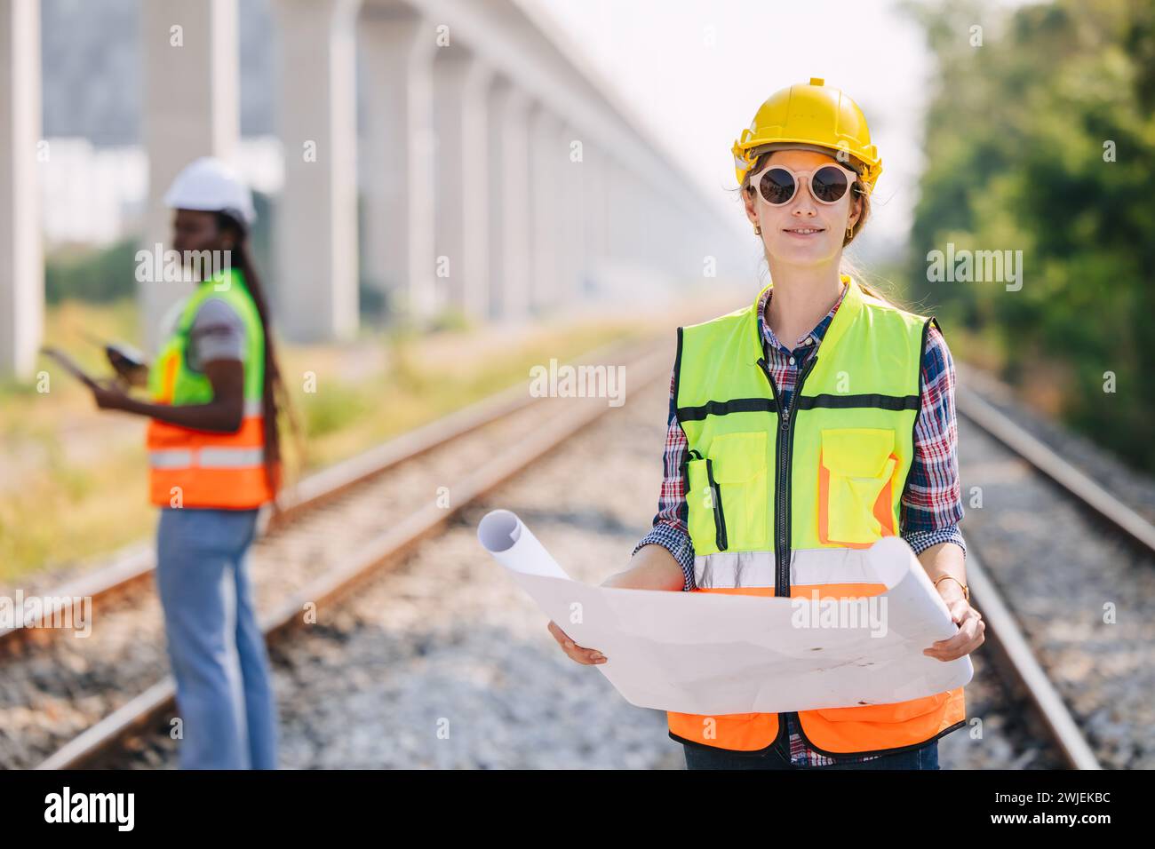 Portrait engineer women on railway tracks construction site with blueprint roll working project manager in suburb transportation line Stock Photo