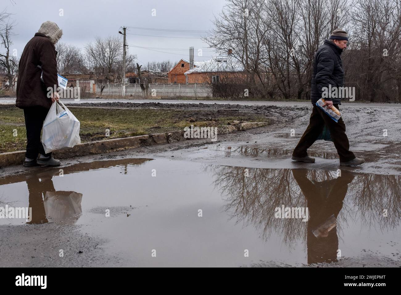 Elderly people walk past a waterlogged area with loaves of bread and
