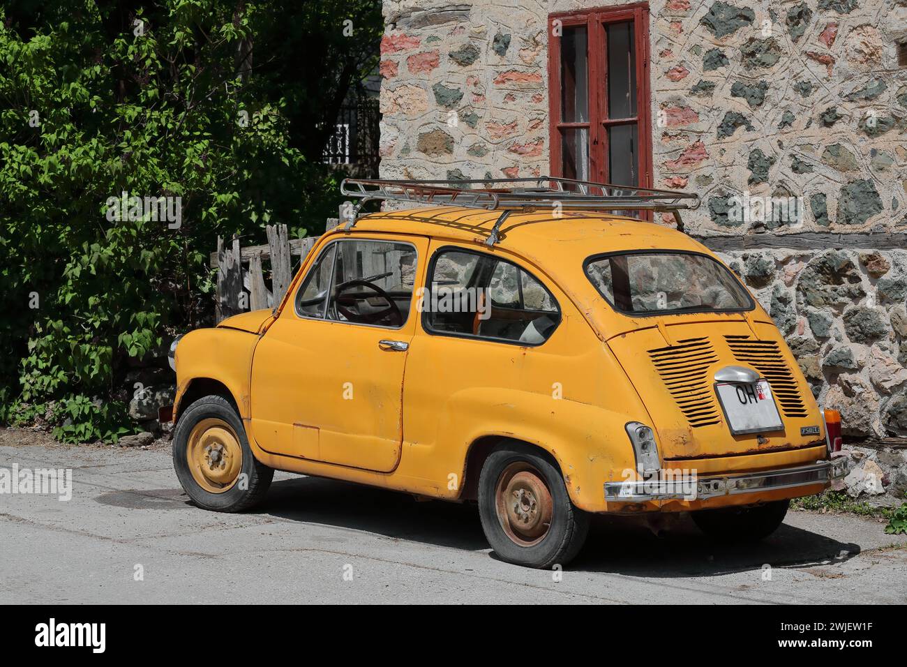 347 Classical Zastava Z750 LE from 1980, orange-yellow colored, so-called Fikjo car, parked in front of a vernacular house. Vevchani-North Macedonia. Stock Photo