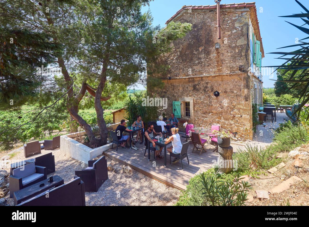 Customers on the terrace of the restaurant “Le Pourquoi pas” in Capestang (south of France), along the Canal du Midi. The Canal du Midi is registered Stock Photo