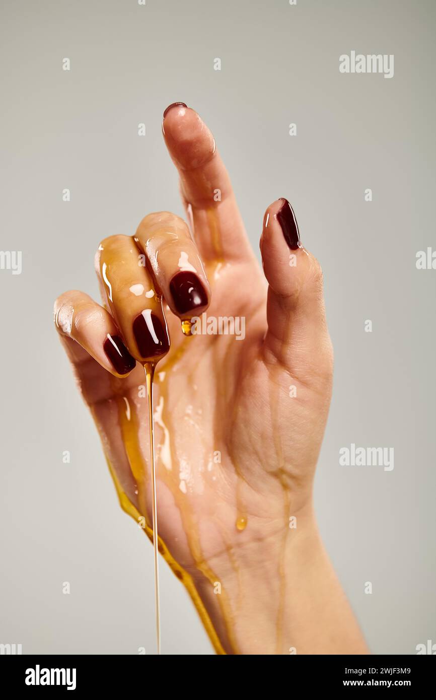 hand of unknown lady pointing up while covered with organic delicious honey on gray backdrop Stock Photo