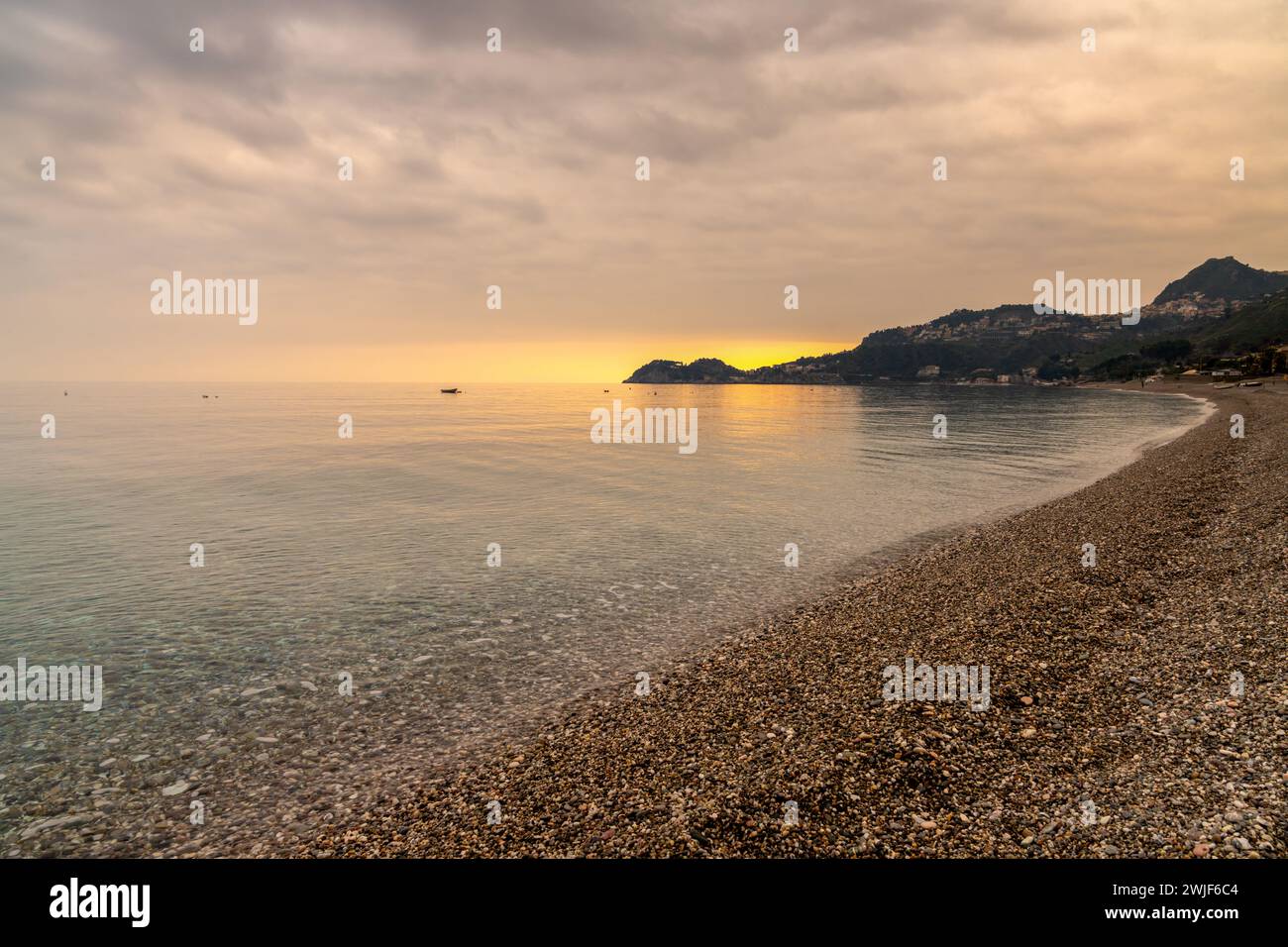 A view of the stone pebble beach and clear water at Letojanni on Sicily at sunsest Stock Photo