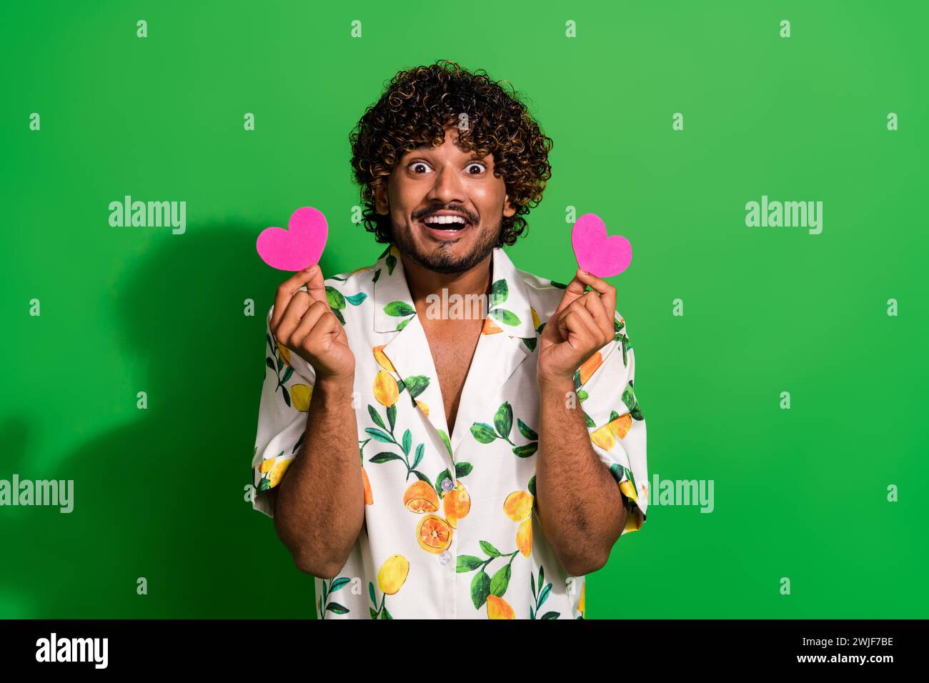 Photo of excited funky arabian man wear print shirt rising two pink heart cards empty space isolated green color background Stock Photo