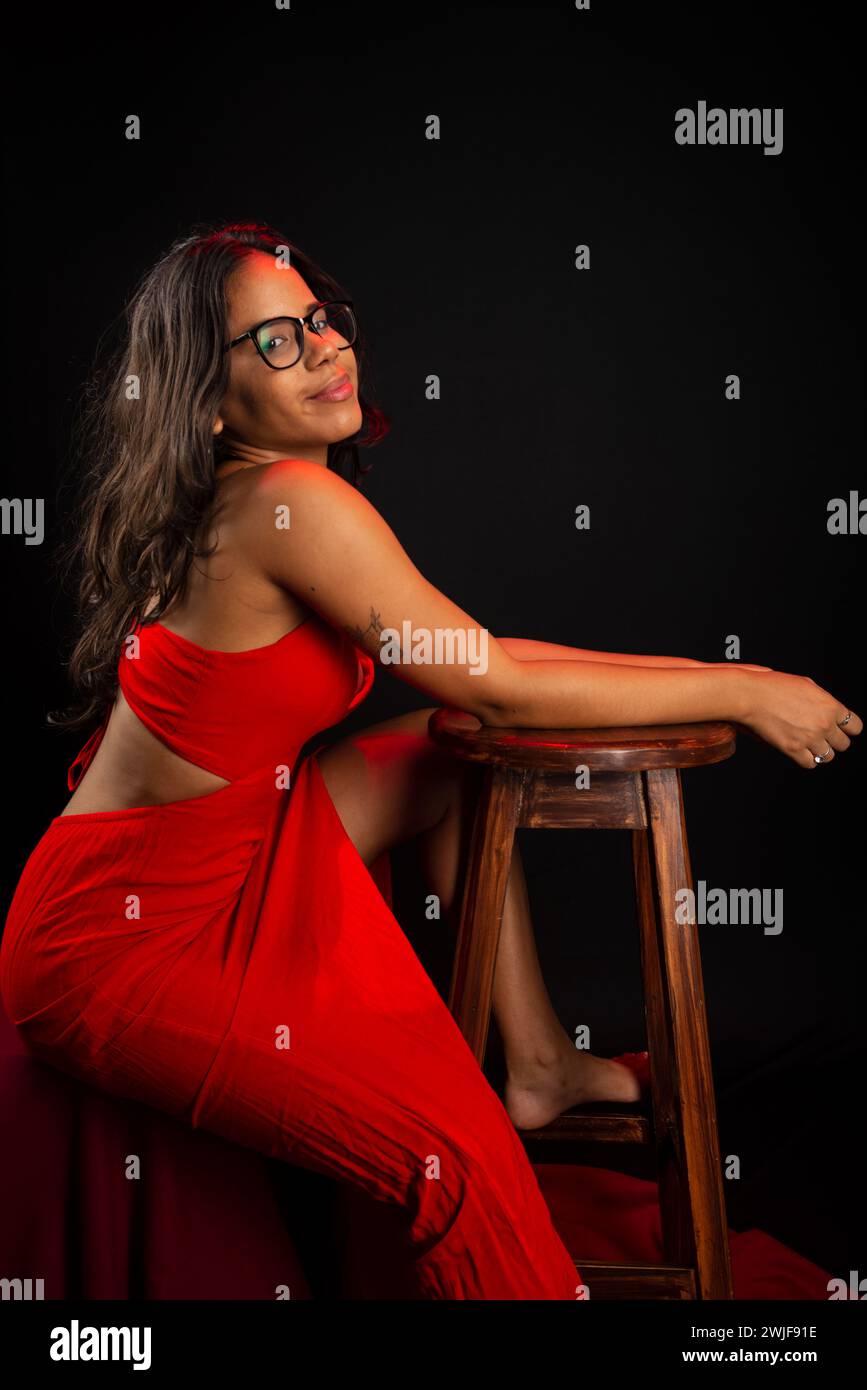 Salvador, bahia, Brazil - December 09, 2023: Portrait of beautiful young woman wearing glasses and in red dress sitting posing for photo. Isolated on Stock Photo