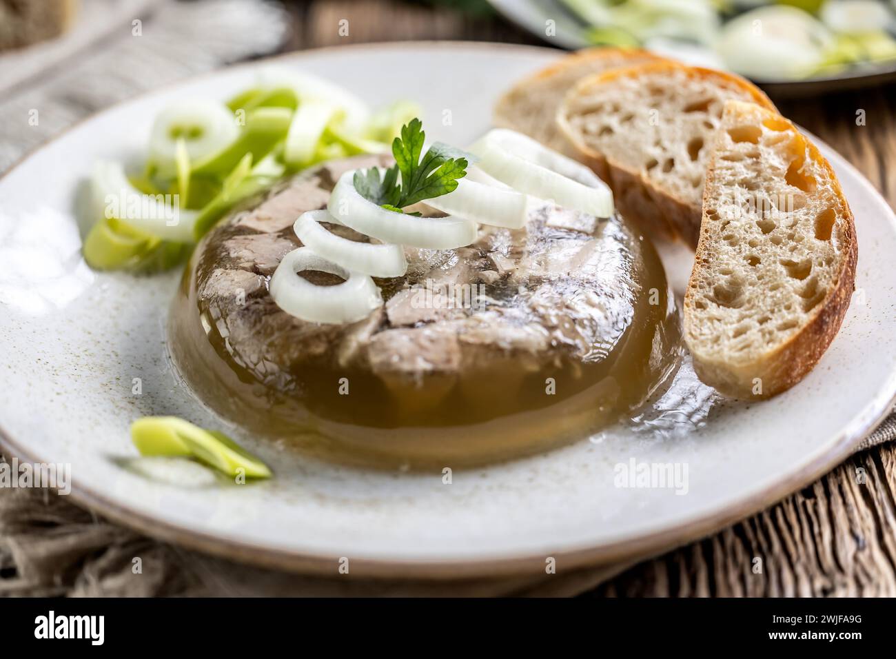 Homemade pork aspic, meat jelly with onion and leek in a white plate. Stock Photo